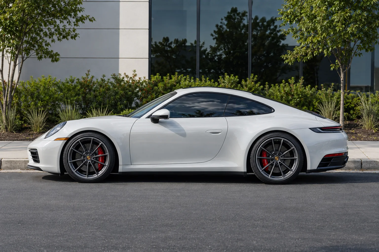 A white Porsche 911 with dark tinted windows parked at a curb on a sunny street