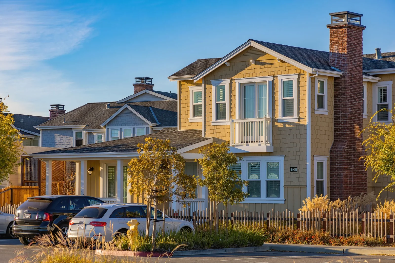 A sunny two-story house with cars parked out front