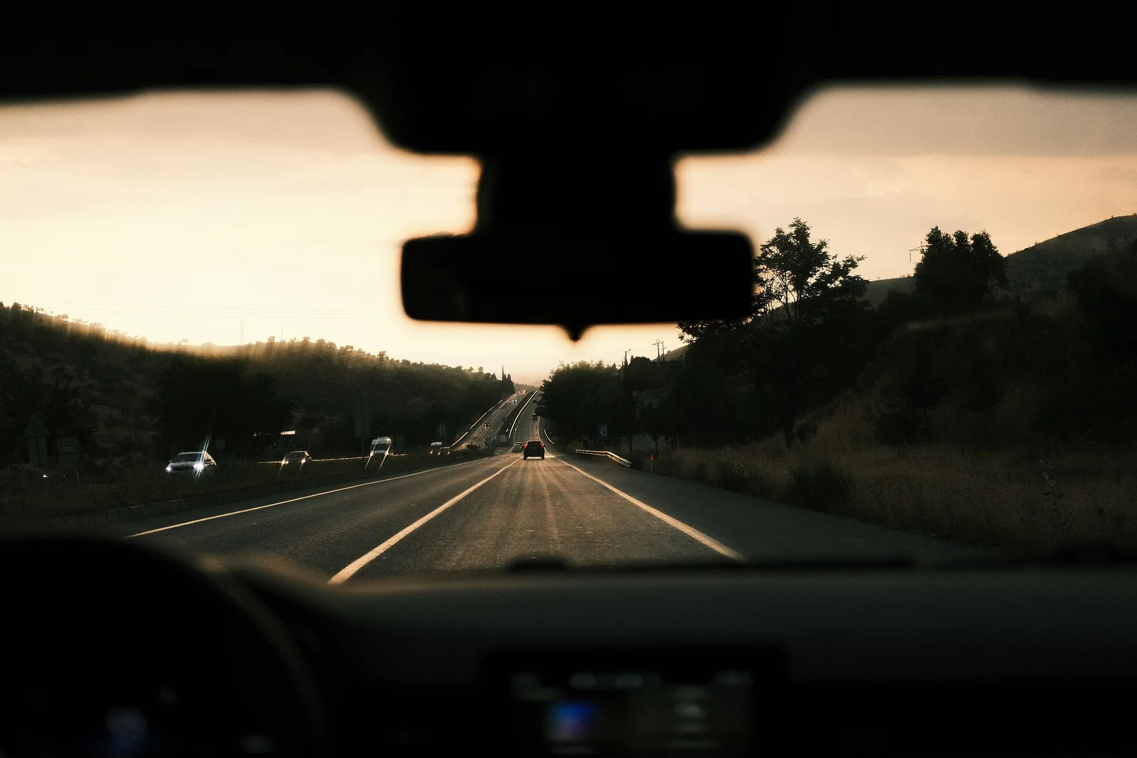 Looking through a windshield down a road into the low evening sun