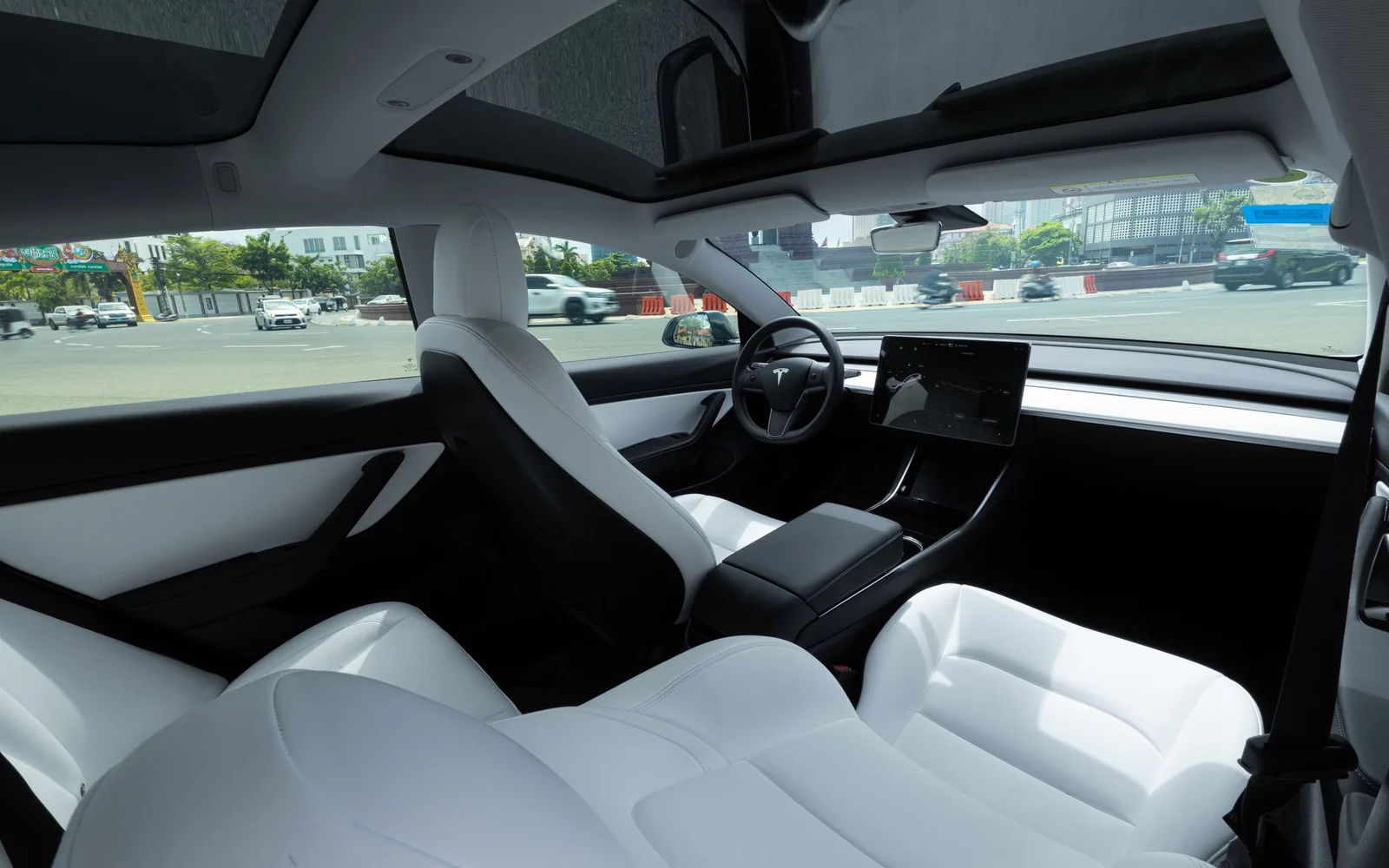 A bright car interior with white seats under a glass roof