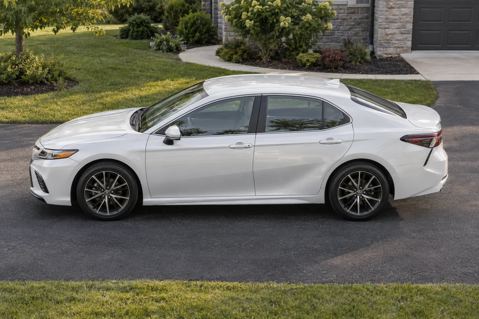 A white Toyota Camry with tinted windows on a home driveway