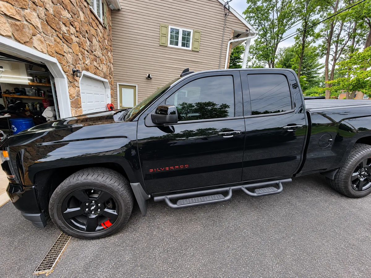 A black Chevrolet Silverado with tinted windows beside a stone garage