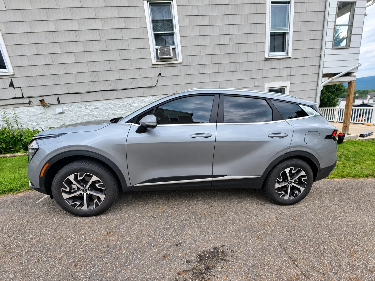 A gray Kia Sportage with tinted windows beside a house
