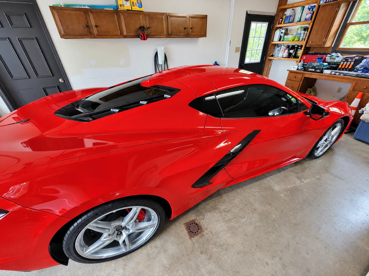 A red Chevrolet Corvette C8 with tinted windows in a garage